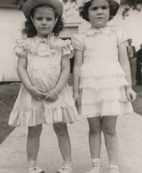 Two girls in matching dresses and hats.